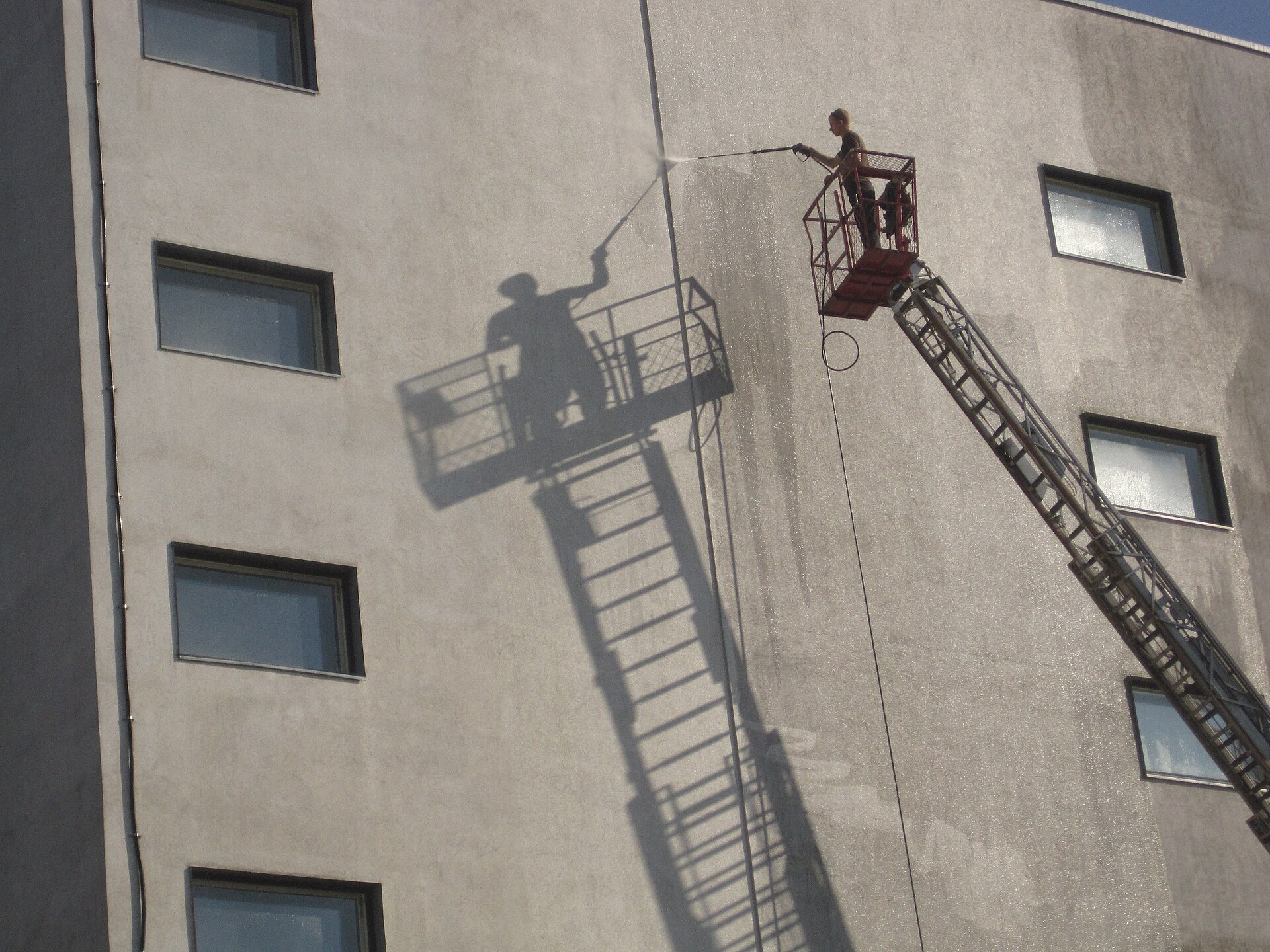 Worker washing a building facade from a lift